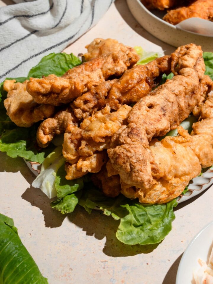A bunch of pieces of crispy chicken tempura on top of lettuce on a plate.