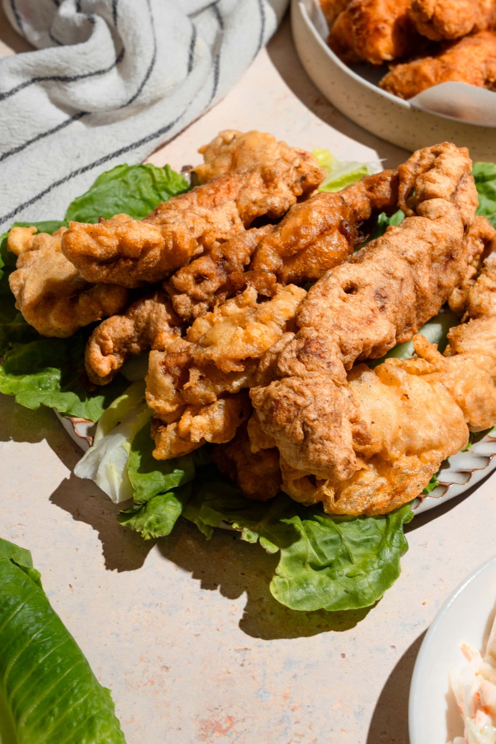A bunch of pieces of crispy chicken tempura on top of lettuce on a plate.