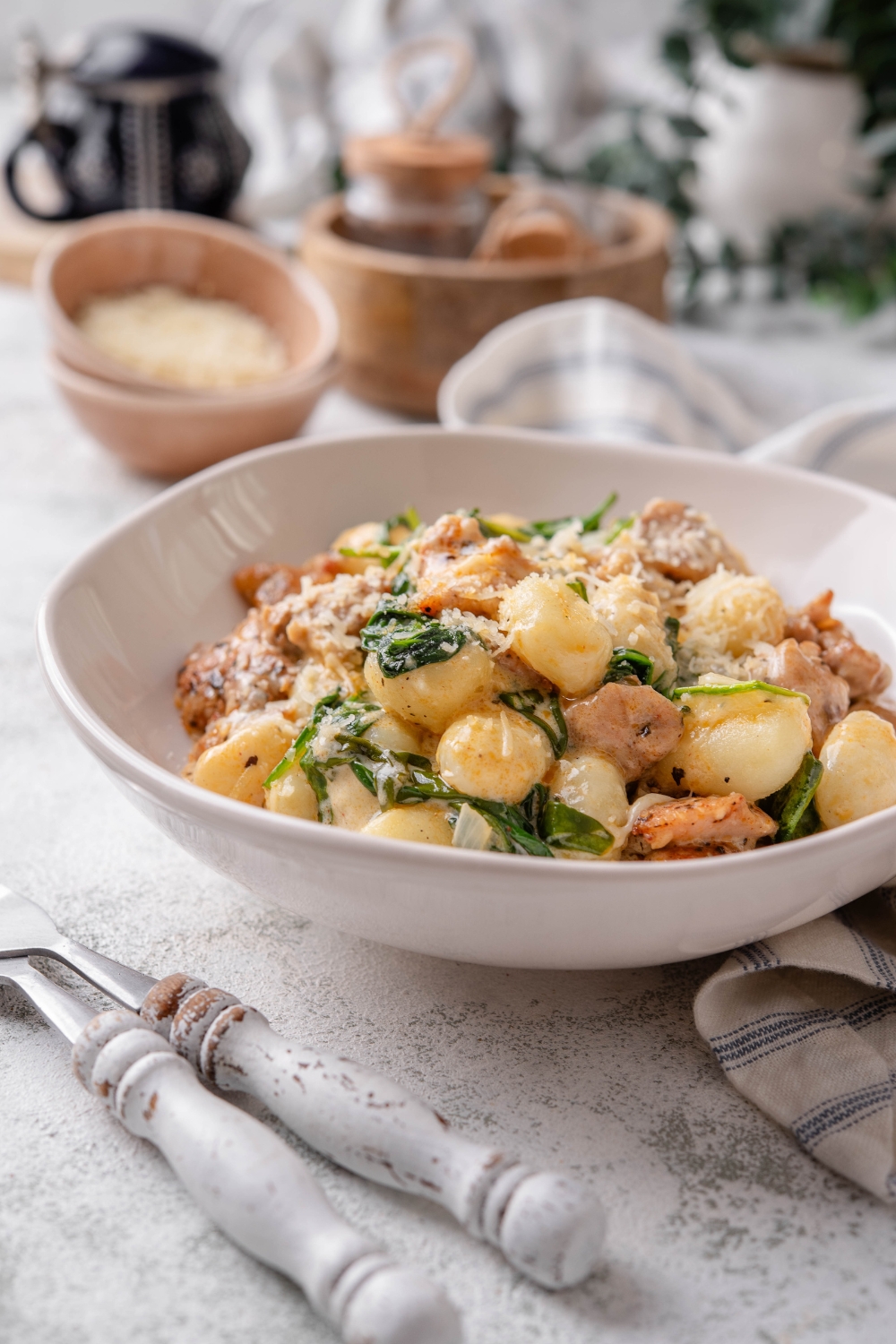 A plate of gnocchi mixed with wilted spinach and chopped pieces of chicken in a creamy sauce.