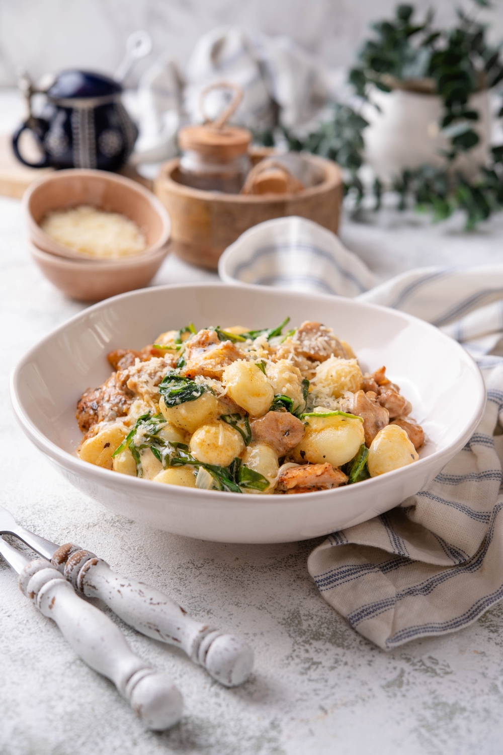 A plate of gnocchi mixed with wilted spinach and chopped pieces of chicken in a creamy sauce with cheese on top.