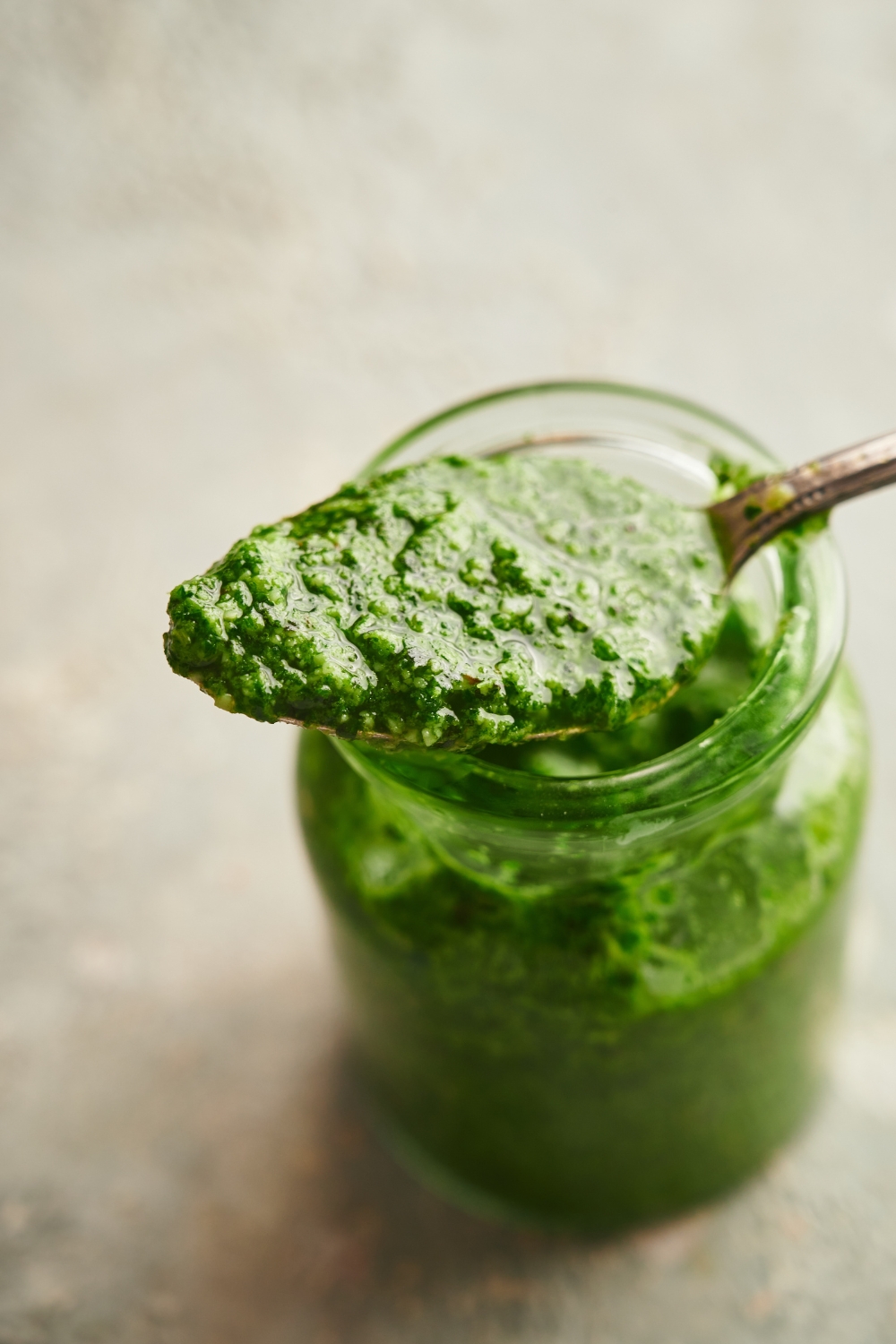 A spoonful of pesto resting on top of a jar of pesto.