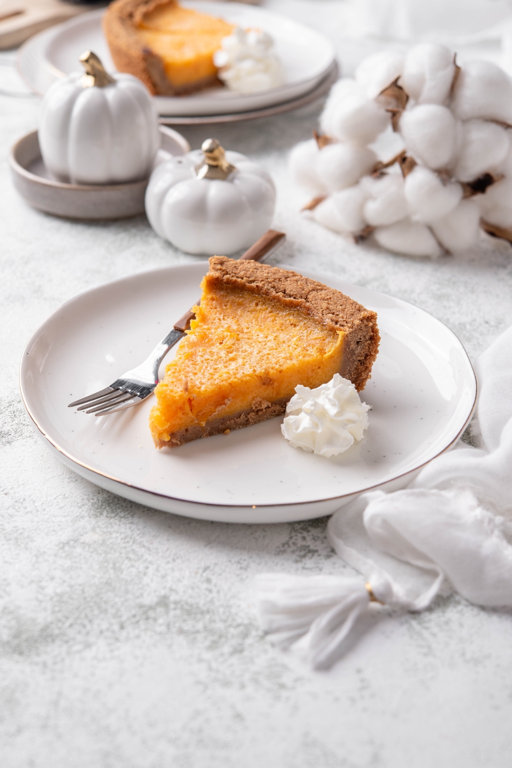 A slice of pumpkin pie on graham cracker crust with a dollop of whipped cream and a fork on the plate.