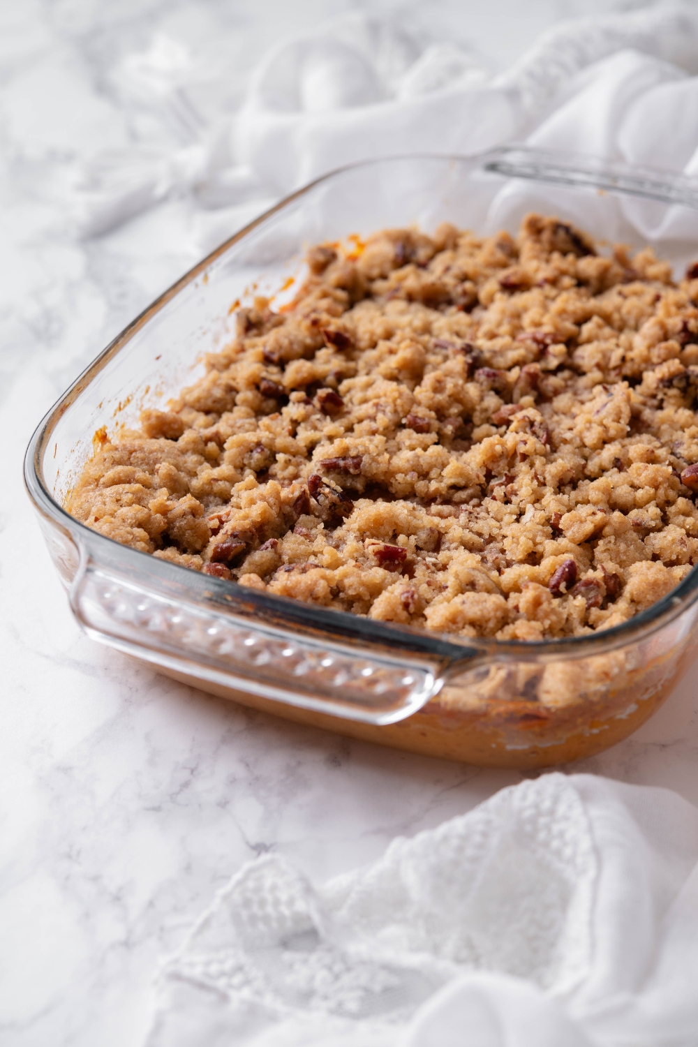 A clear baking dish filled with casserole covered in a pecan and brown sugar topping.