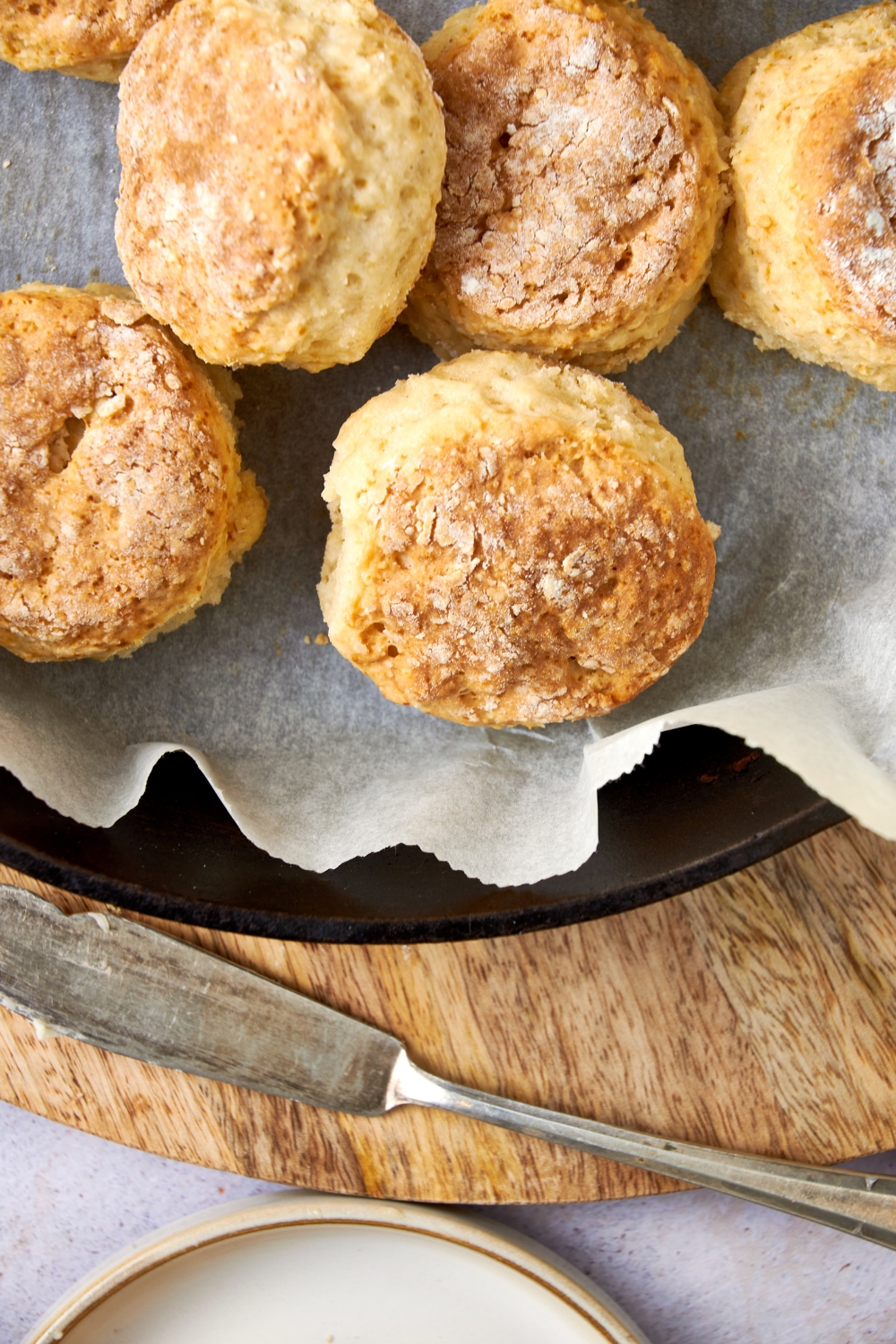Golden brown cathead biscuits in a parchment paper lined pan with a serving knife on a wooden board nearby.