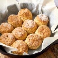 Ten golden brown Cathead biscuits in a parchment paper lined pan on a wooden counter.