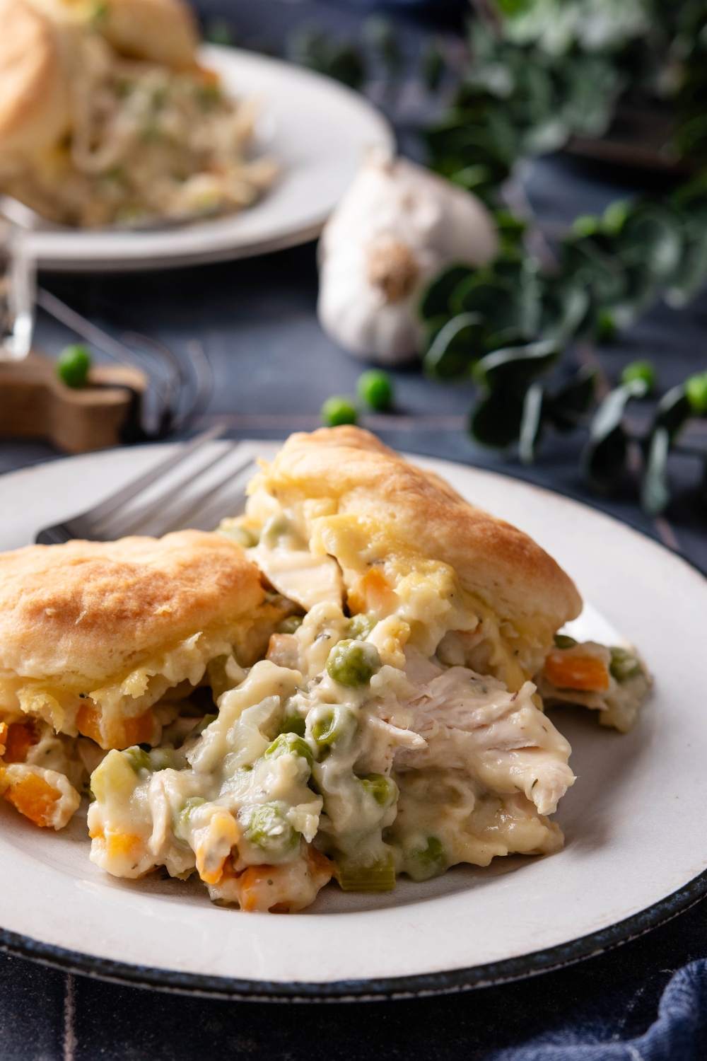 A white plate full of chicken pot pie and biscuits on a black counter top.