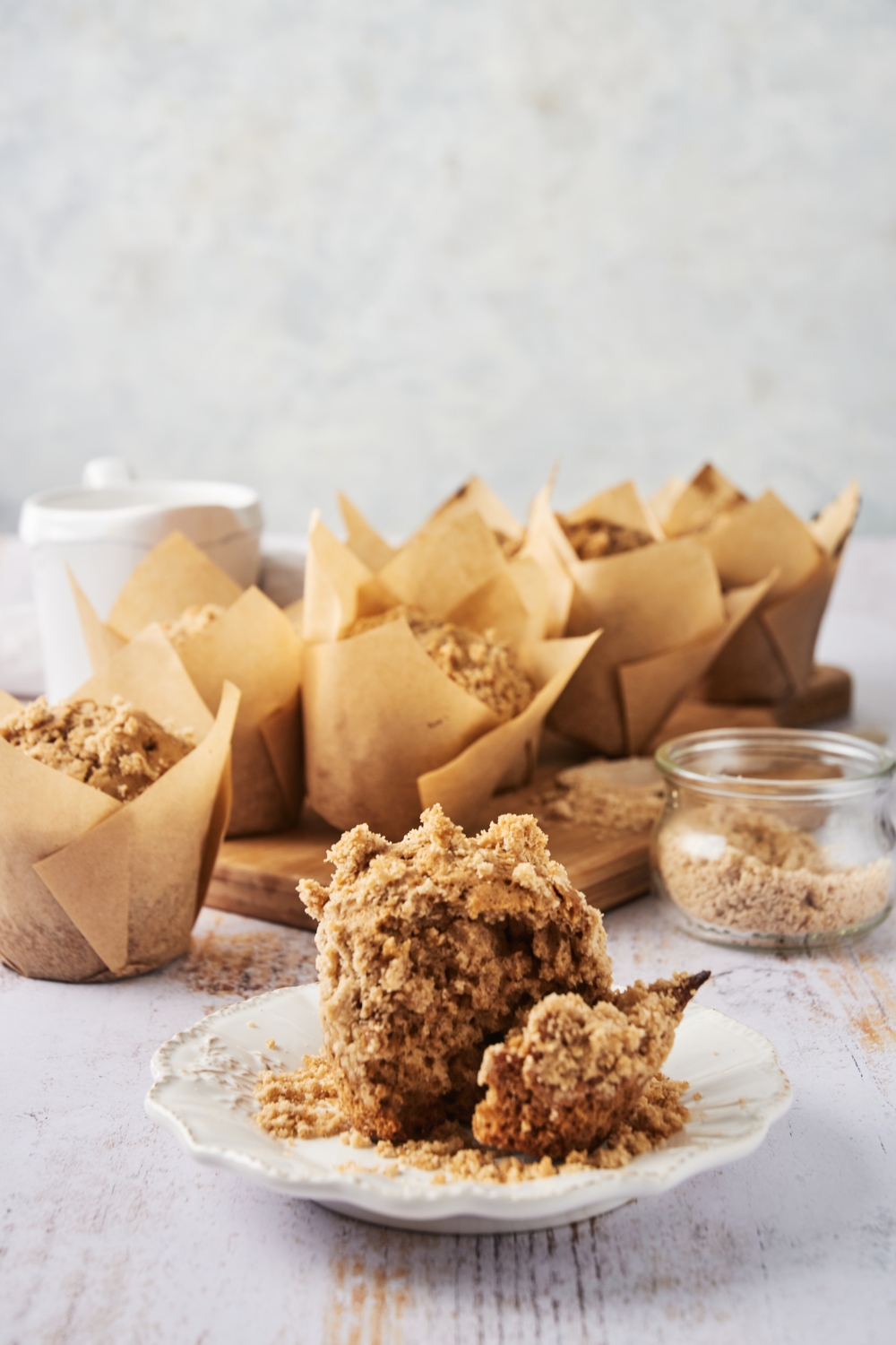 A plate with a cinnamon streusel muffin. A serving board with the remaining muffins are behind the plate.