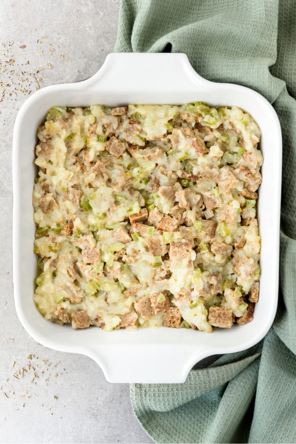 A casserole dish full of cooked Amish potato stuffing on a gray counter with a green dish towel.