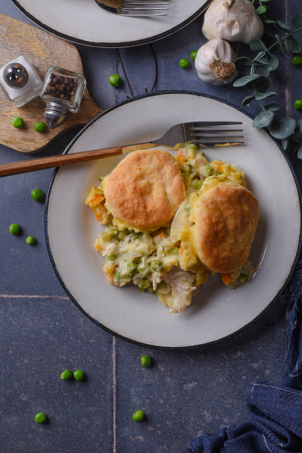 A top down view of a full plate of chicken pot pie and biscuits with a fork on a black counter top.