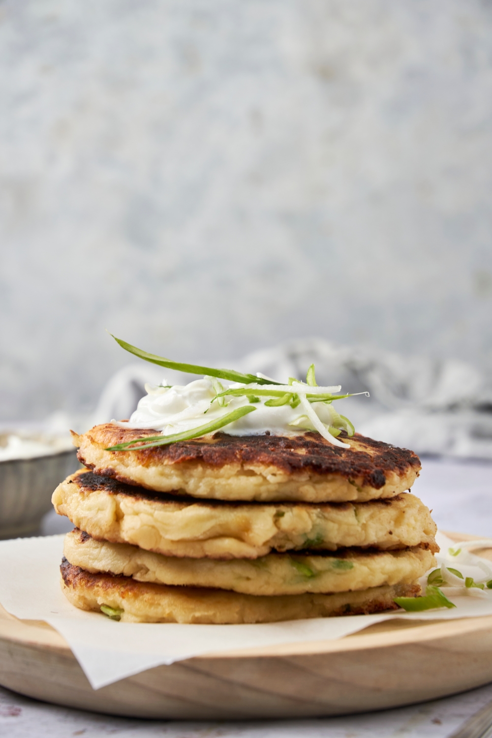 A stack of four potato pancakes on a plate with sour cream and green onion on top.