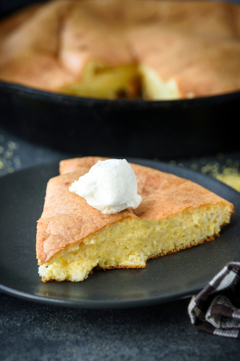 A slice of cornbread topped with cream cheese sits on a black plate.
