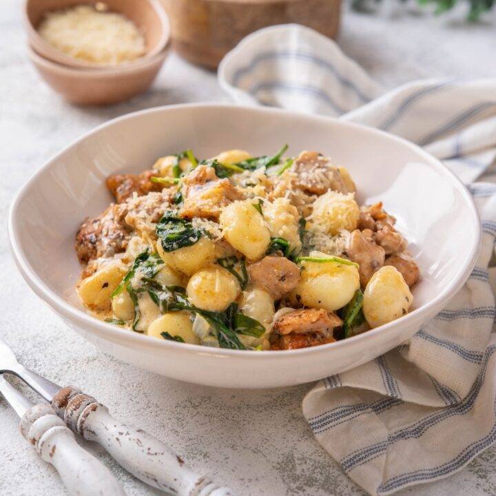 A plate of gnocchi mixed with wilted spinach and chopped pieces of chicken in a creamy sauce.