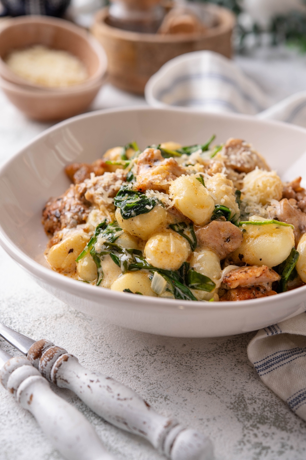 A plate of gnocchi mixed with wilted spinach and chopped pieces of chicken in a creamy sauce.