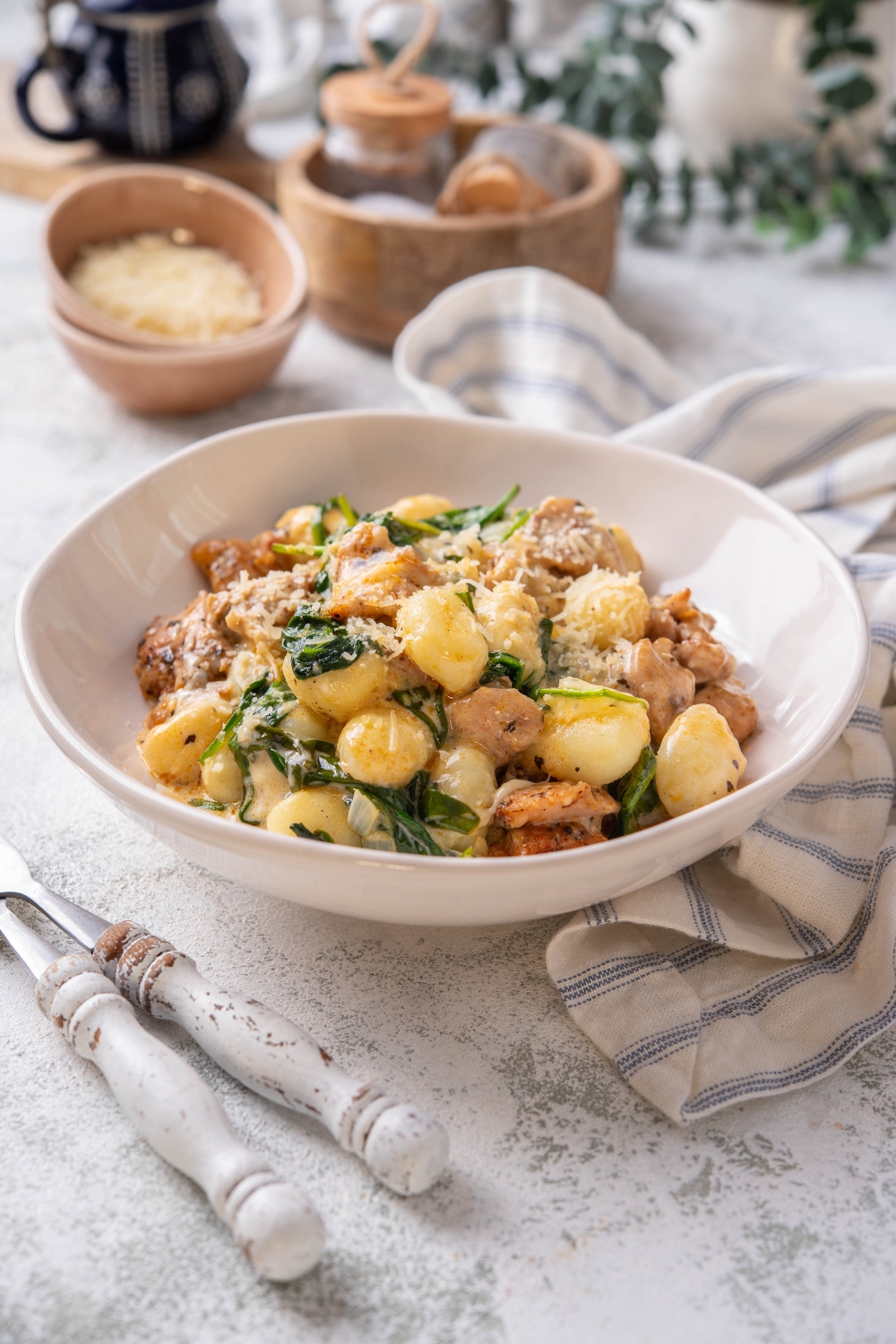 A plate of gnocchi mixed with wilted spinach and chopped pieces of chicken in a creamy sauce.