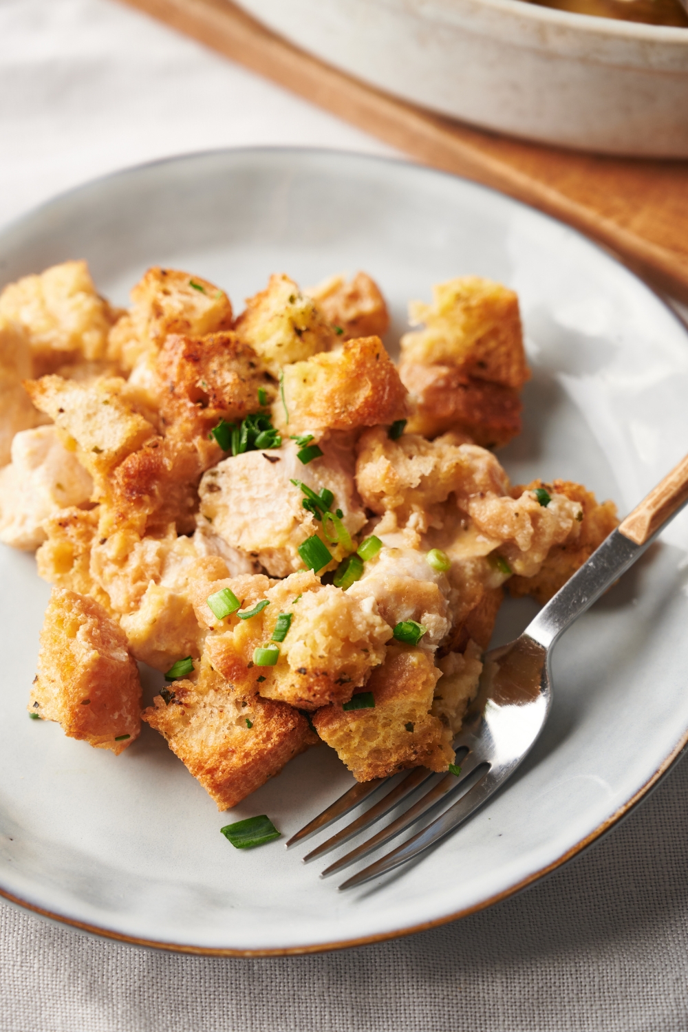 A plate of chicken stuffing casserole garnished with fresh green herbs and a fork is on the plate.