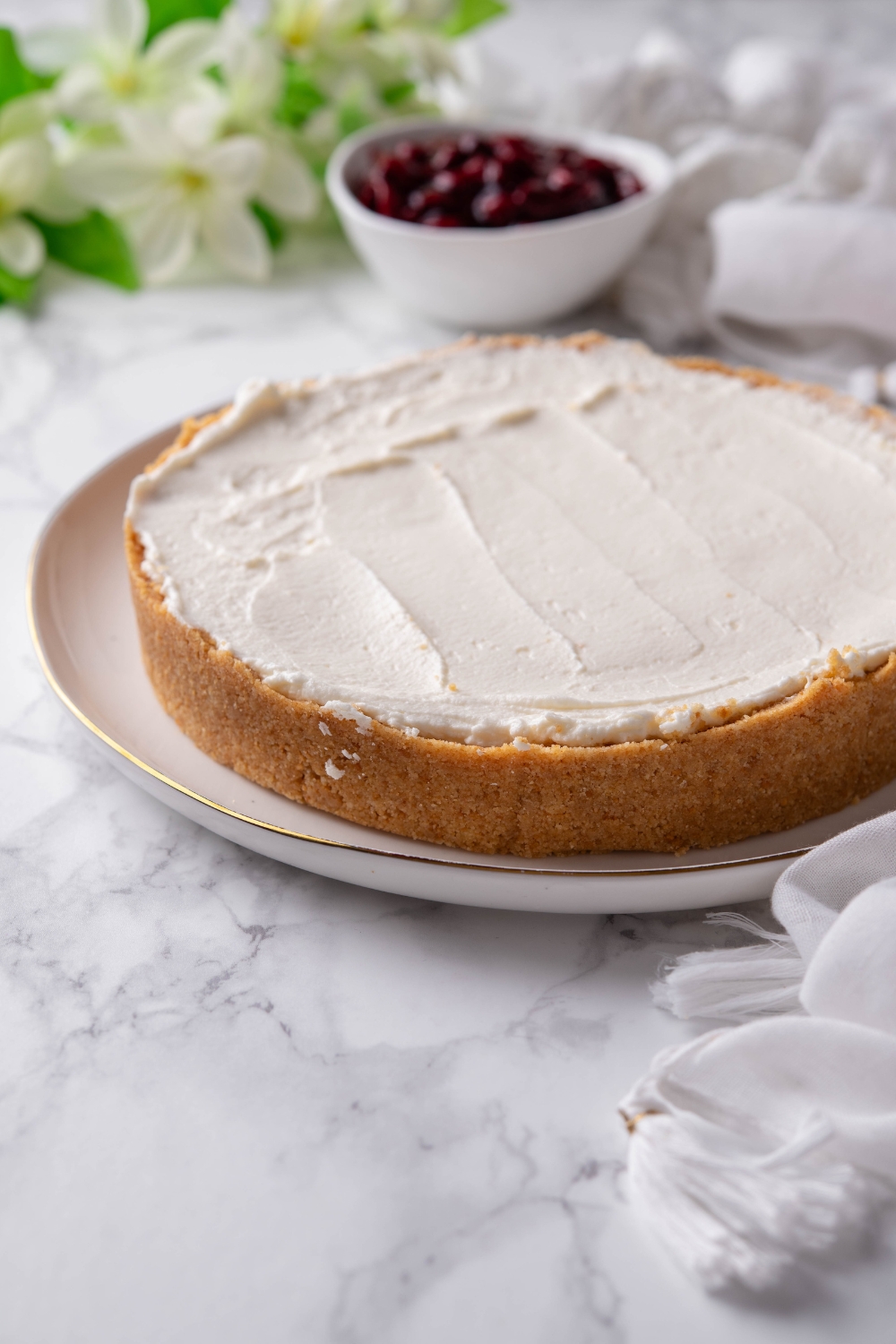 A cream cheese pie on a white plate with a bowl of cherry pie filling in the background.