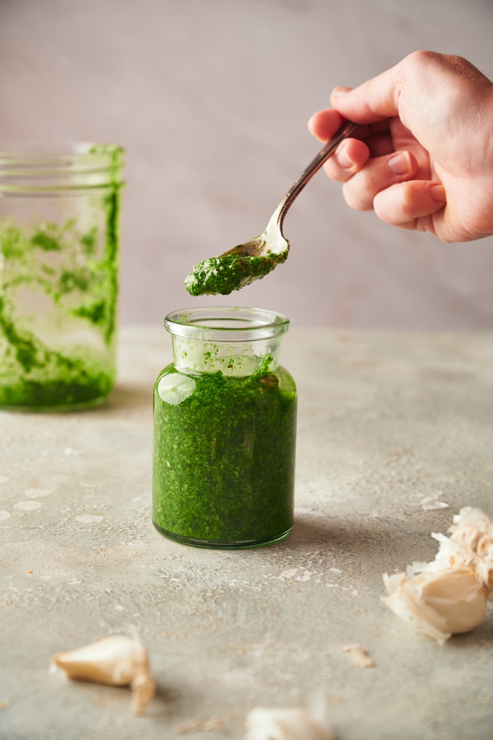 A spoonful of pesto held above a jar of pesto.