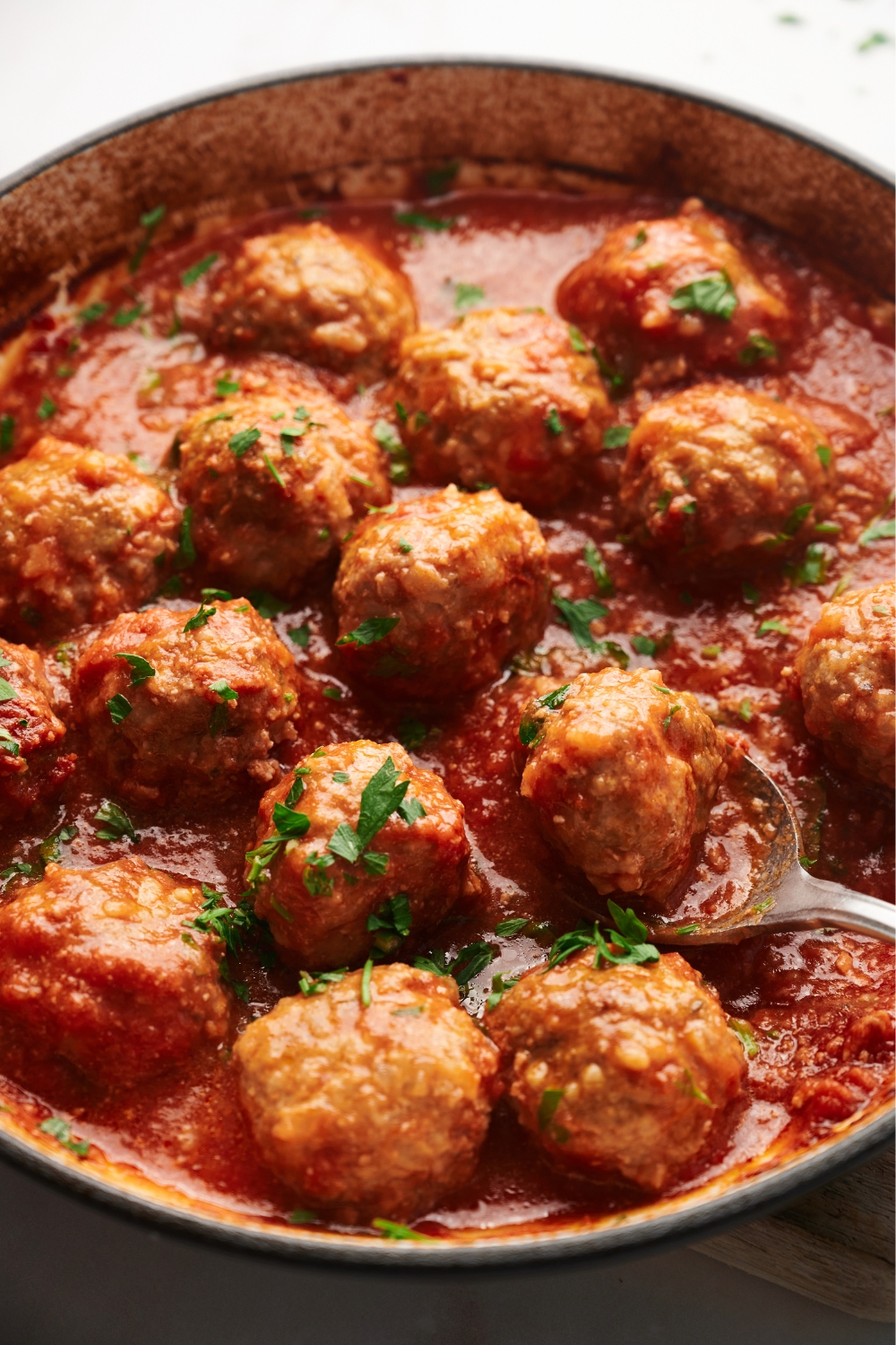 cooked meatballs in a pot with a silver spoon and parsley