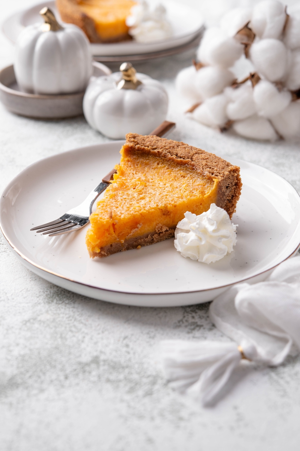 A slice of pumpkin pie on graham cracker crust with a dollop of whipped cream and a fork on the plate.