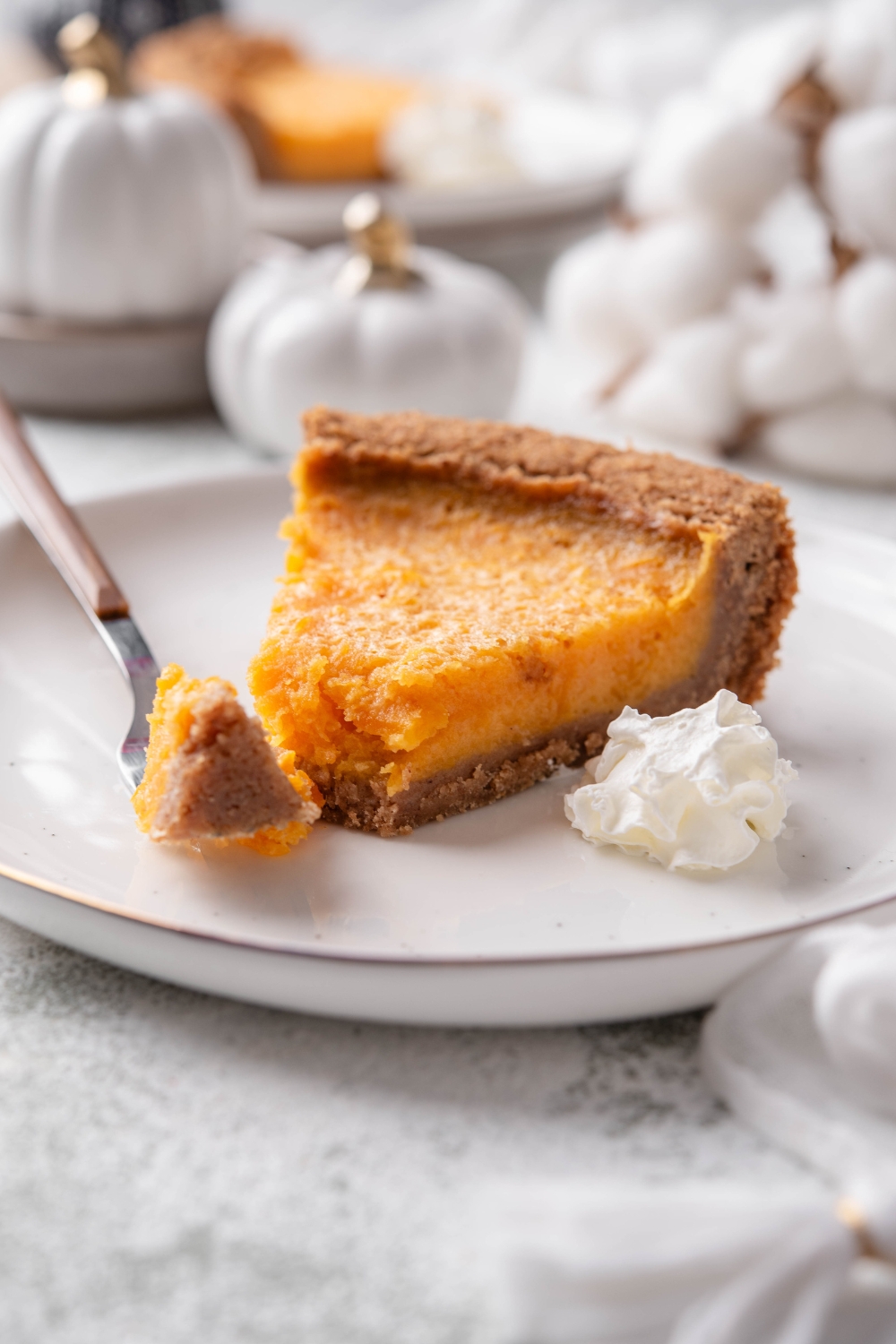 A slice of pumpkin pie on graham cracker crust with a fork on the plate holding a piece of the pumpkin pie slice on it.