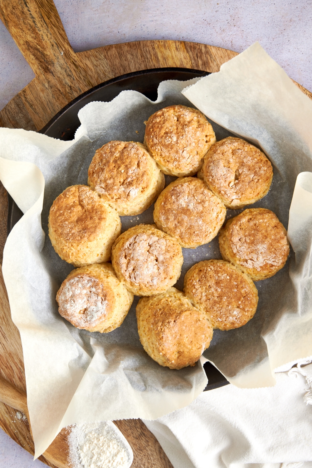 Ten golden brown cathead biscuits in a parchment paper lined pan on a wooden serving board.