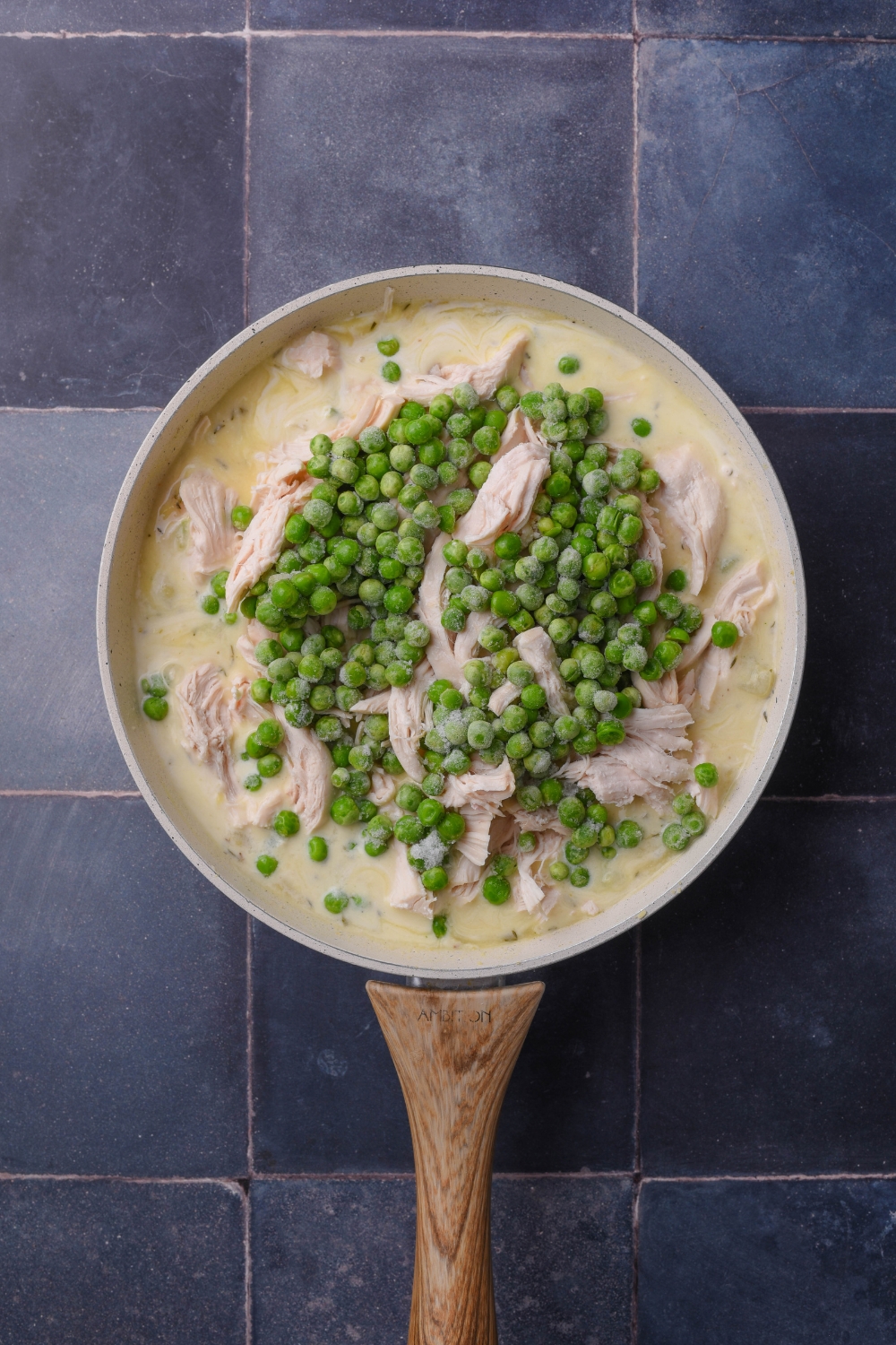 Shredded chicken and frozen peas in a white sauce pan full of chicken pot pie filling.