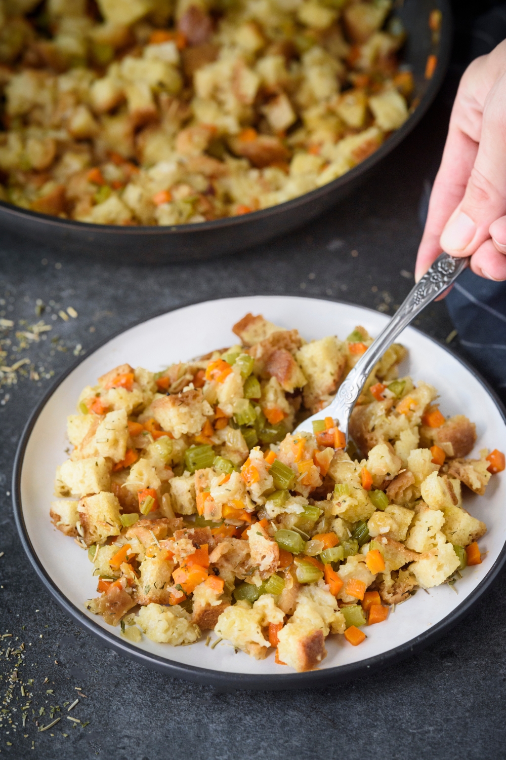 A plate of stovetop stuffing with diced celery and carrots mixed in with the stuffing. A fork is grabbing a bite of stuffing.