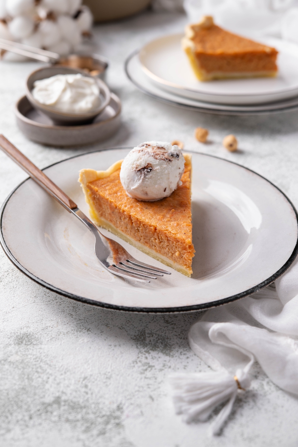 A slice of sweet potato pie on a plate with a dollop of whipped cream on top and a fork on the plate next to it.