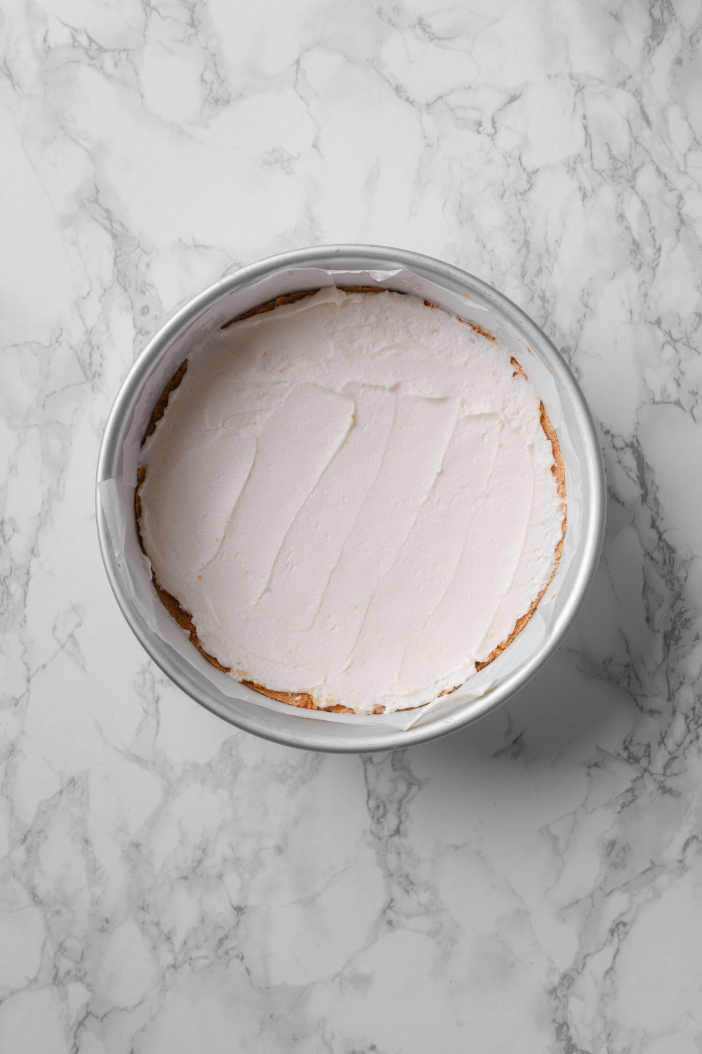 A circular pan lined with parchment paper with a cream cheese pie in it.