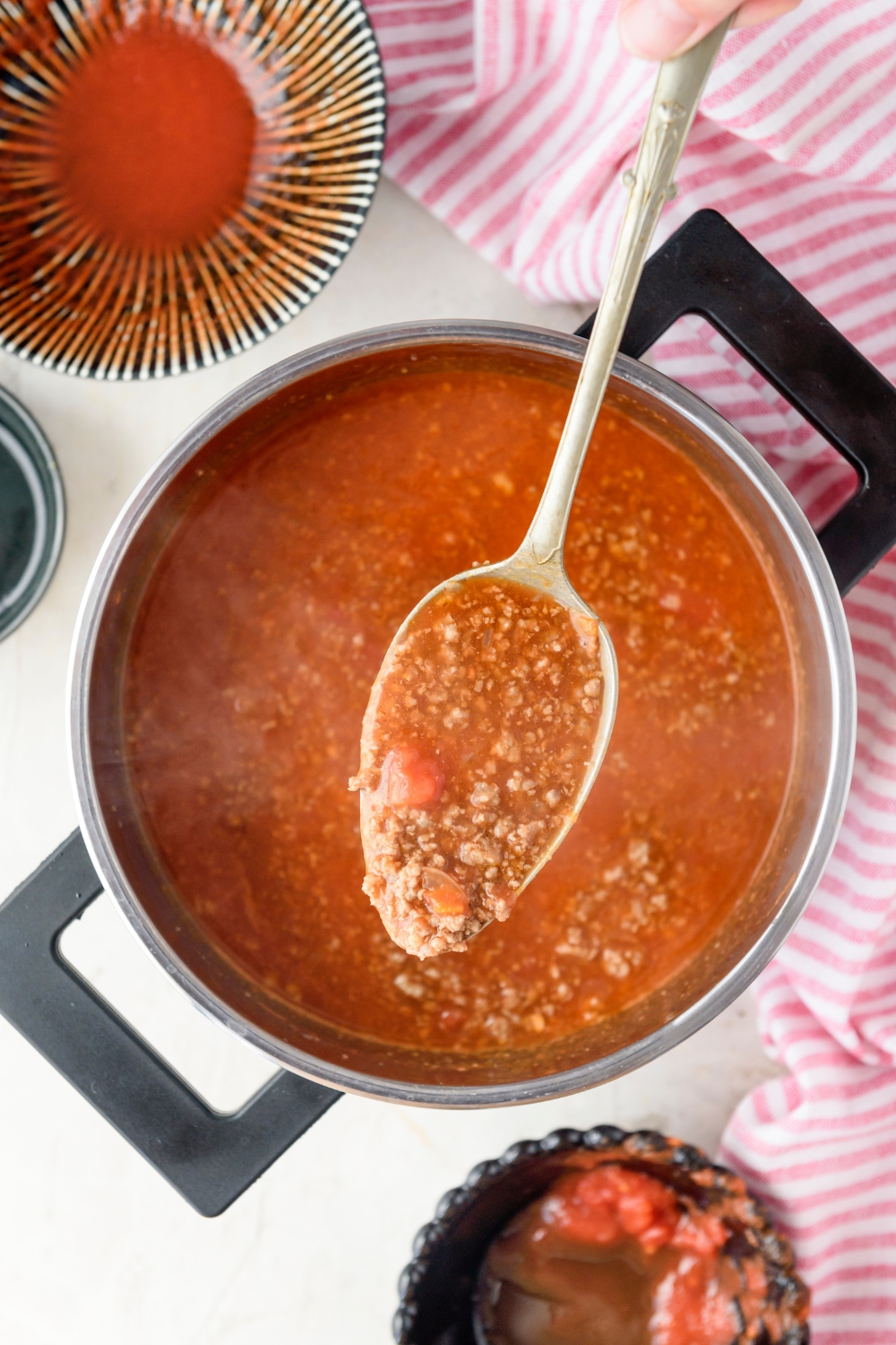 A spoonful of ground beef in tomato sauce held above a pot filled with more ground beef and sauce.