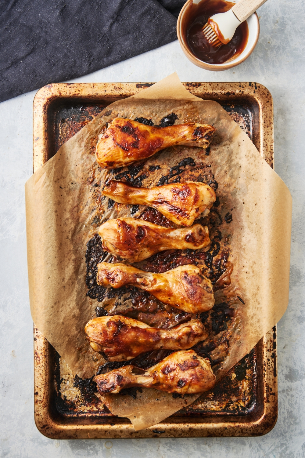 A baking sheet lined with parchment paper with six chicken drumsticks covered in barbecue sauce.