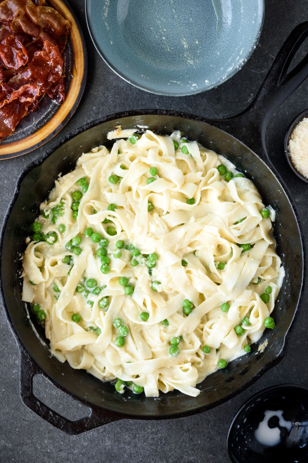 A cast iron skillet filled with cooked pasta mixed with peas in a creamy sauce.