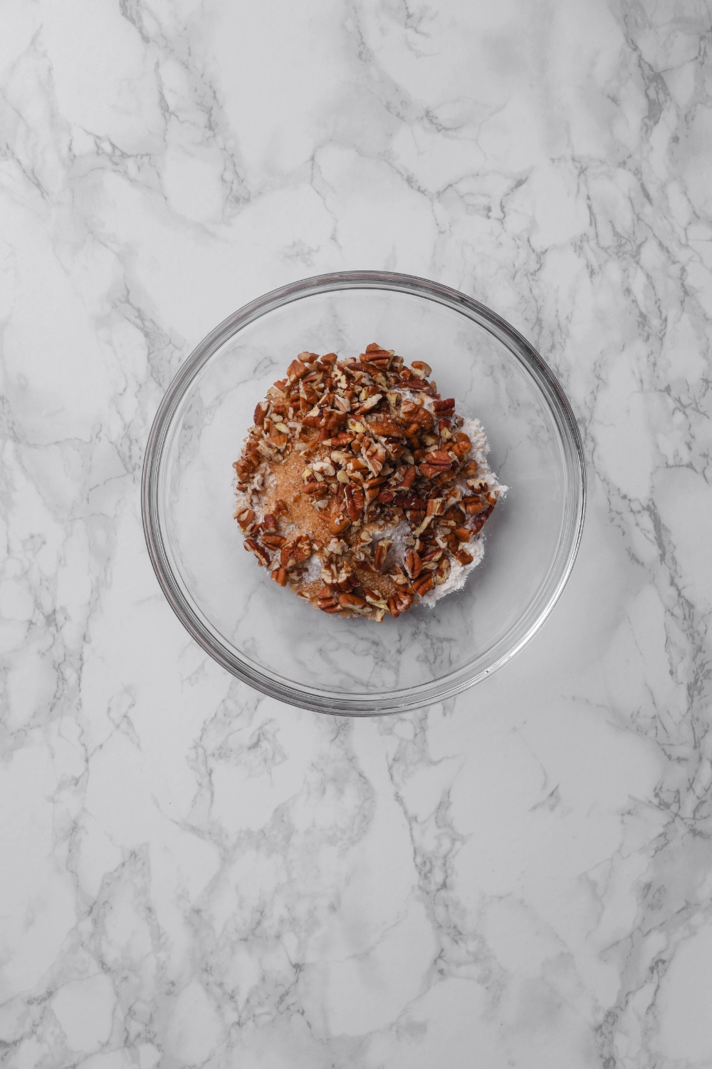A clear bowl filled with chopped pecans, brown sugar, and flour.