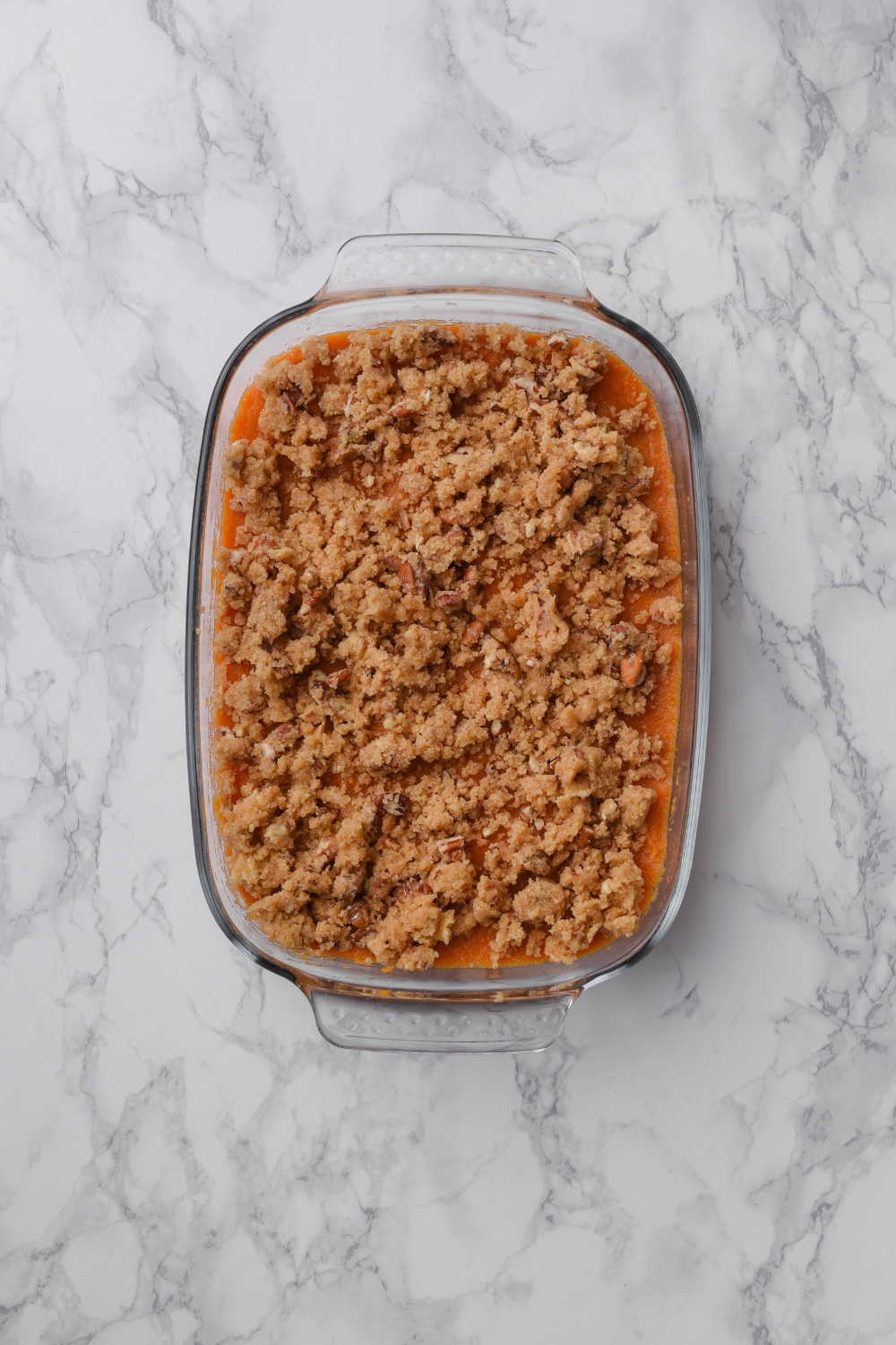 A clear baking dish filled with sweet potato puree and a pecan and brown sugar topping.