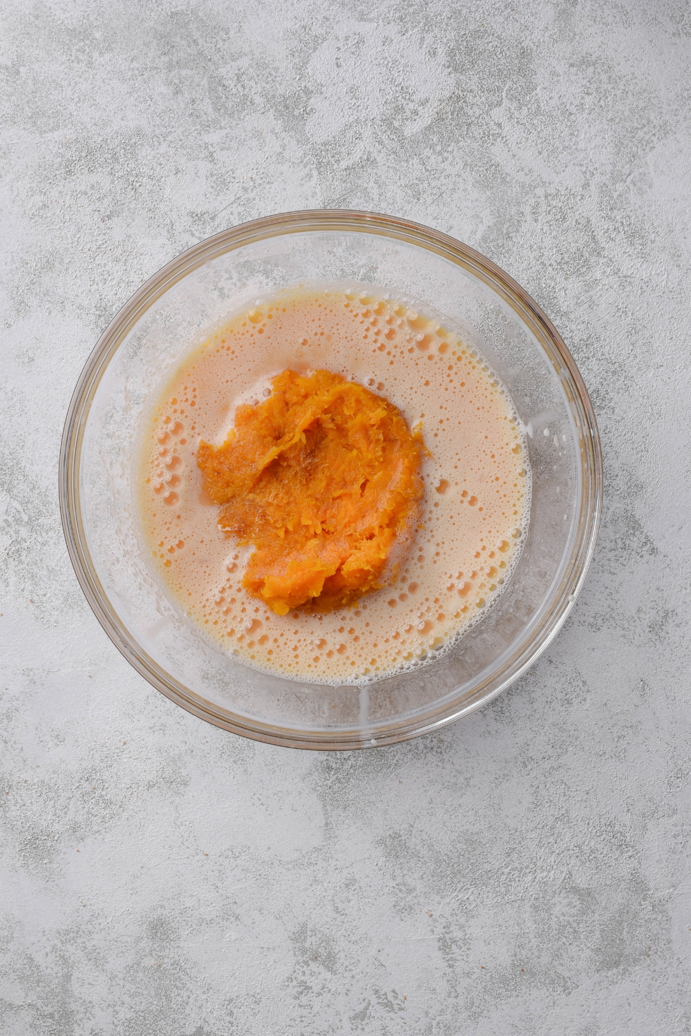 A clear bowl with a beaten egg mixture and a scoop of pumpkin puree in the bowl.