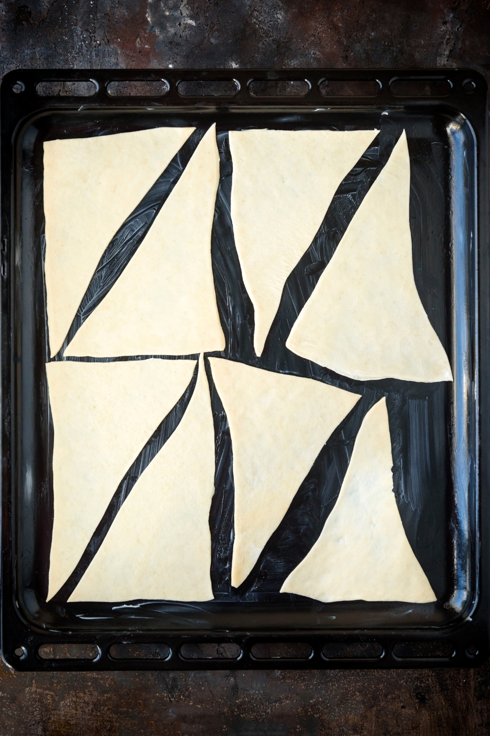 Eight triangles of crescent dough are laying on a black baking pan.