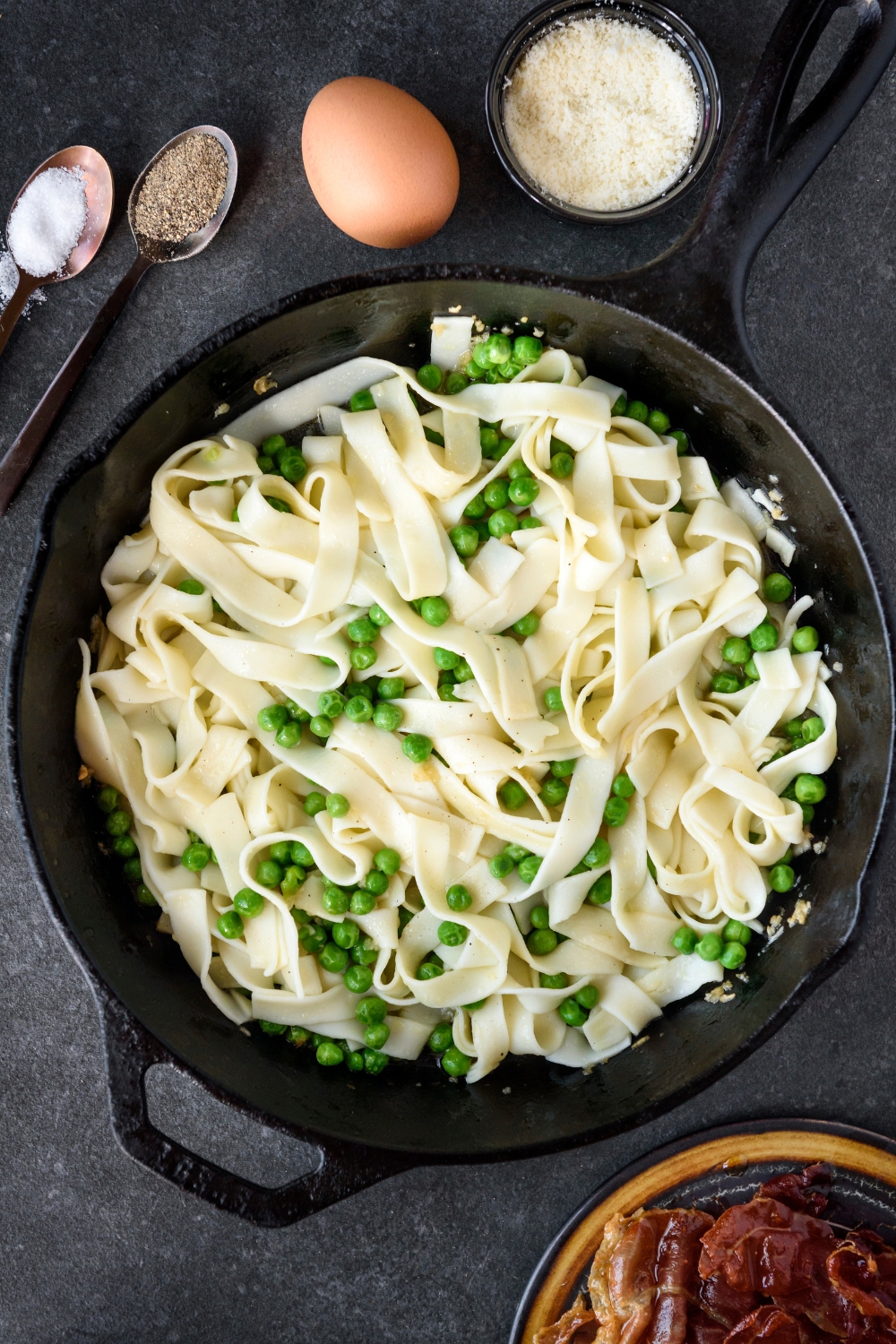 A cast iron skillet filled with cooked pasta mixed with peas.