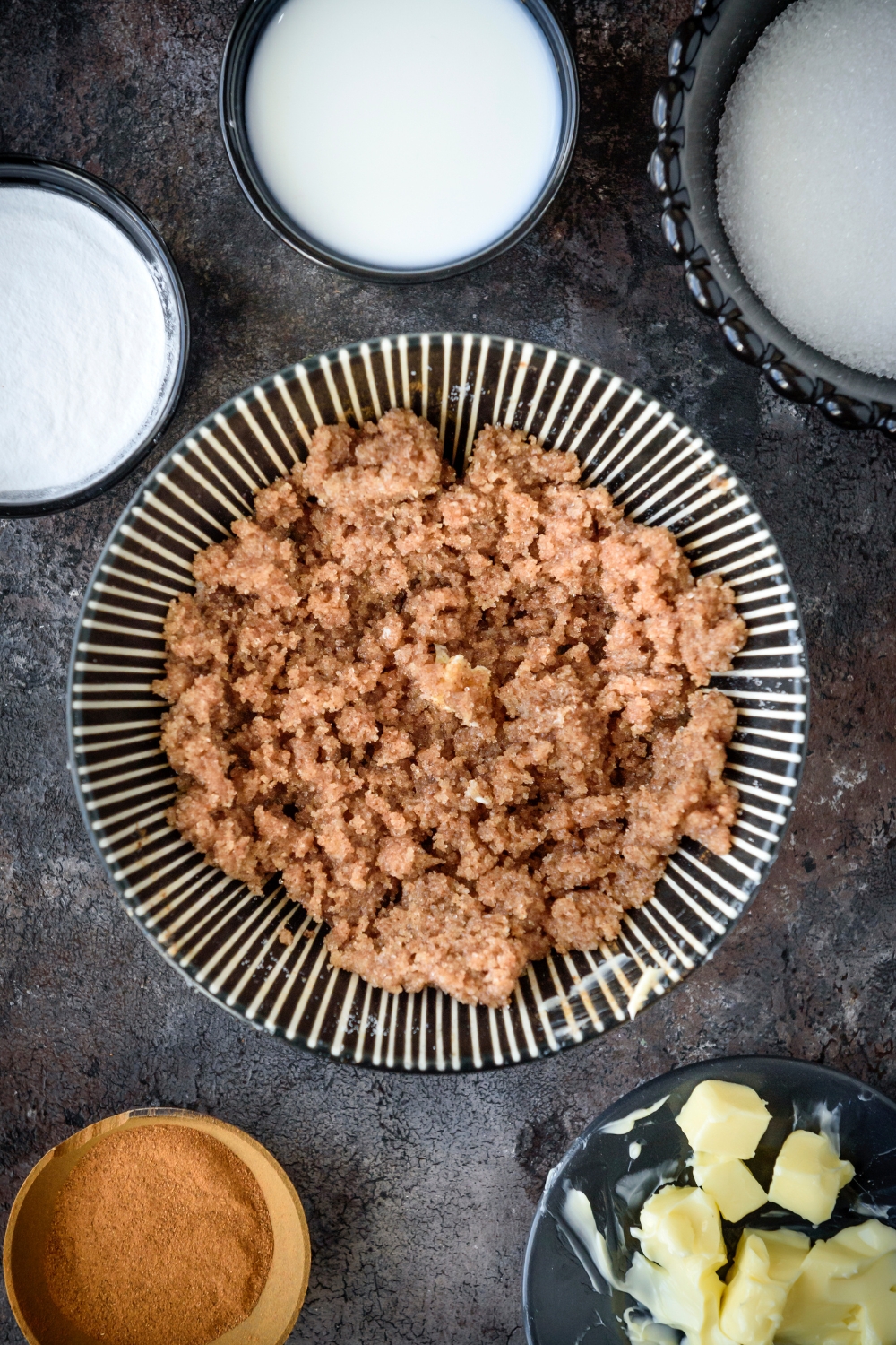 Cinnamon and sugar filling on a black and white plate. Bowls of butter, cinnamon, sugar, milk, and powdered sugar are nearby.