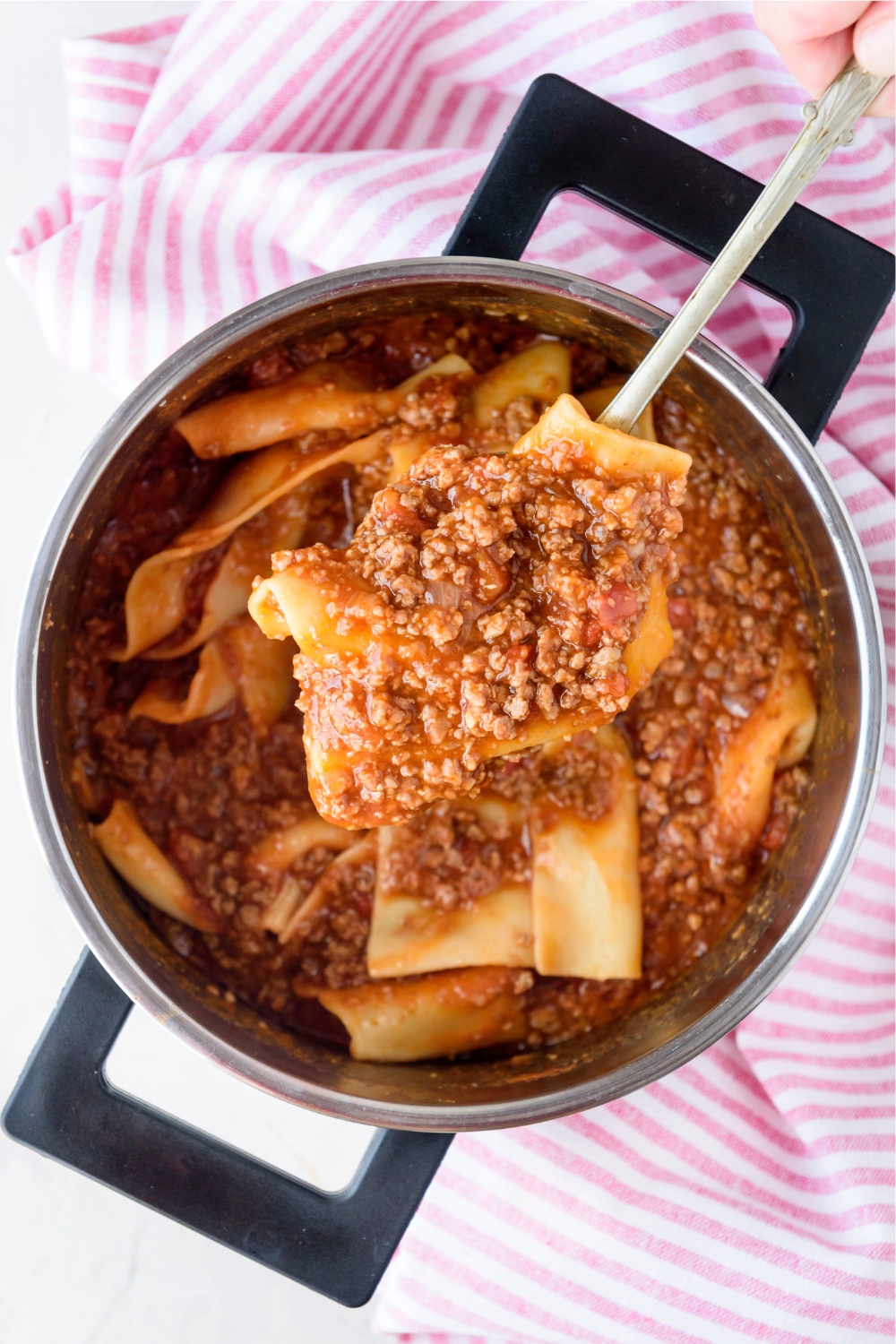 A spoonful of cooked pasta mixed with ground beef in tomato sauce held above a pot filled with more ground beef, pasta, and sauce.