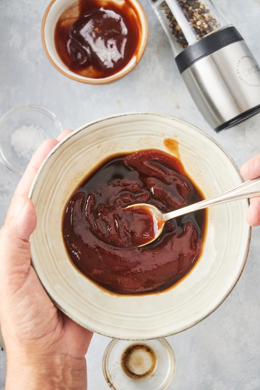 A bowl of barbecue sauce with a spoon in it being held above the countertop.