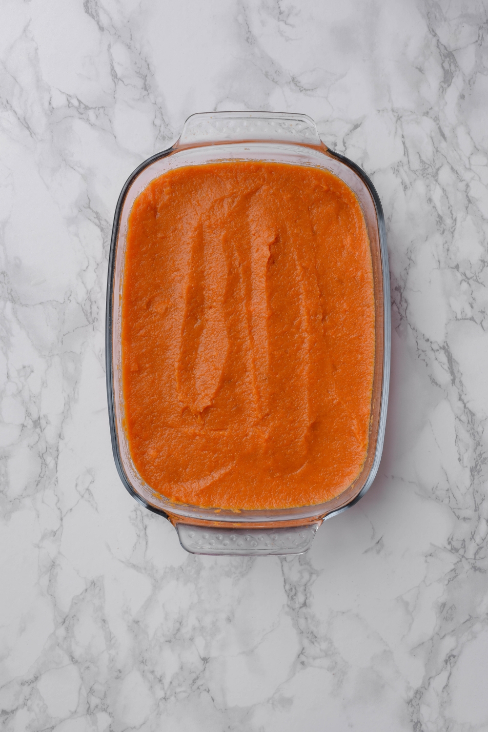 A clear baking dish filled with sweet potato puree that has been spread into an even layer.