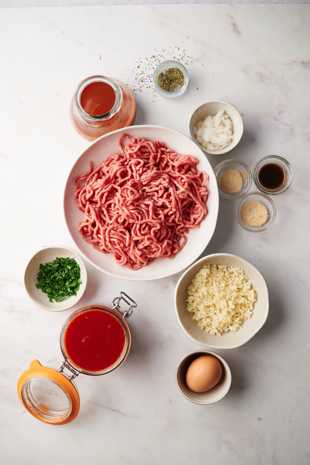 ground beef, rice, tomato sauce, parsley, an egg, and spices in separate bowls on a white counter