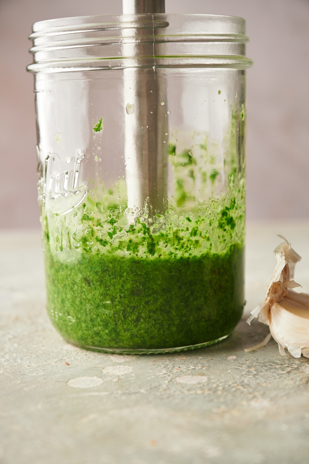 A mason jar filled with pesto and an immersion blender is blending the pesto.