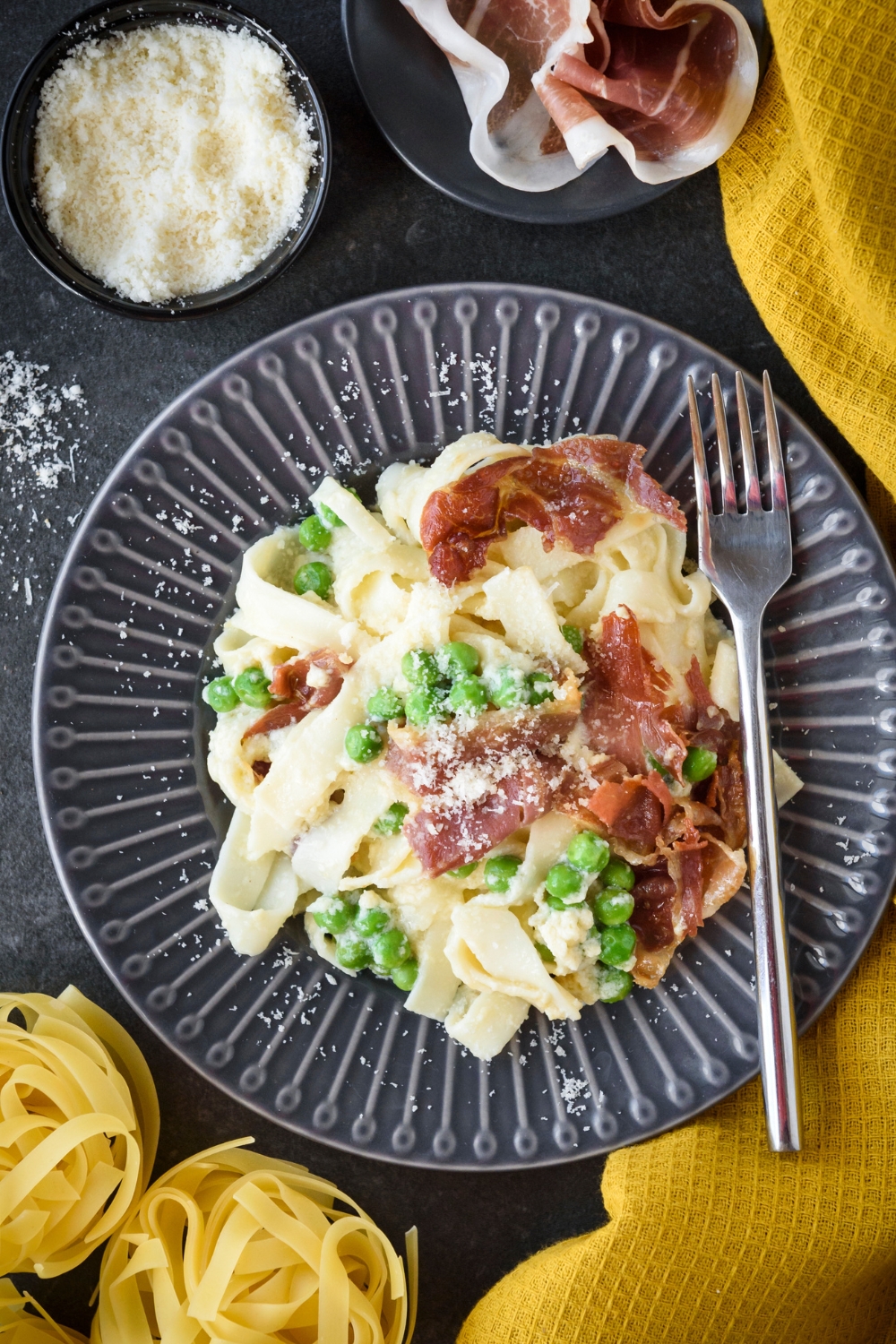A plate filled with cooked pasta mixed with peas and prosciutto in a creamy sauce with cheese on top.