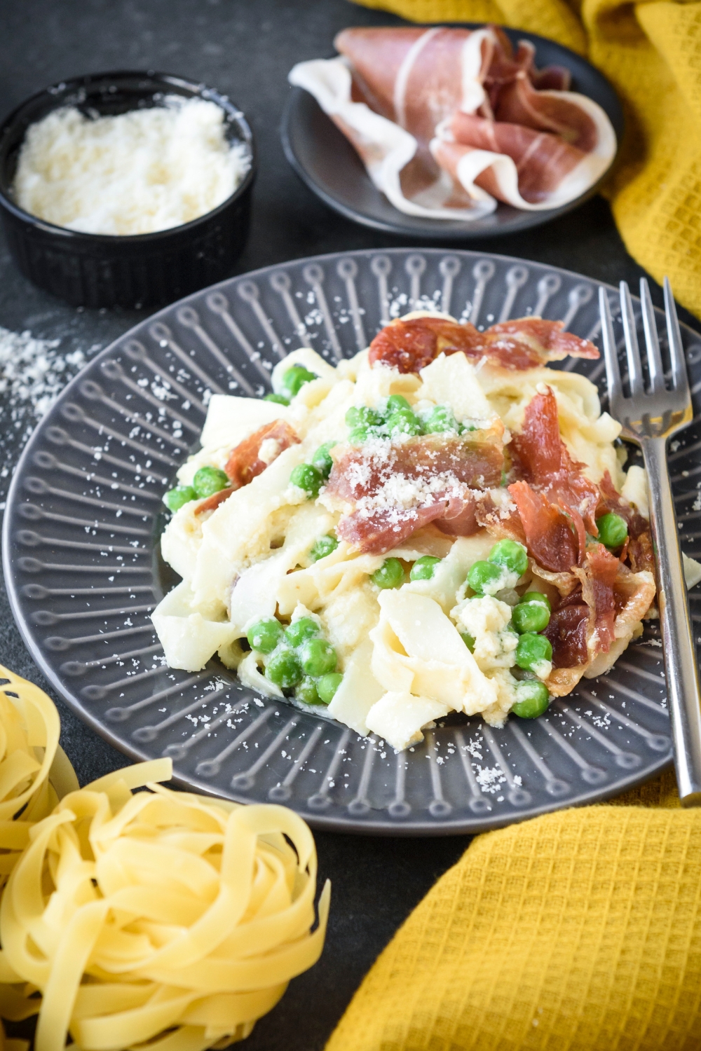 A plate filled with cooked pasta mixed with peas and prosciutto in a creamy sauce with cheese on top.