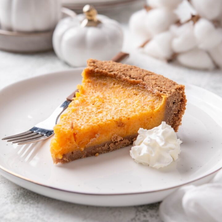 A slice of pumpkin pie on graham cracker crust with a dollop of whipped cream and a fork on the plate.