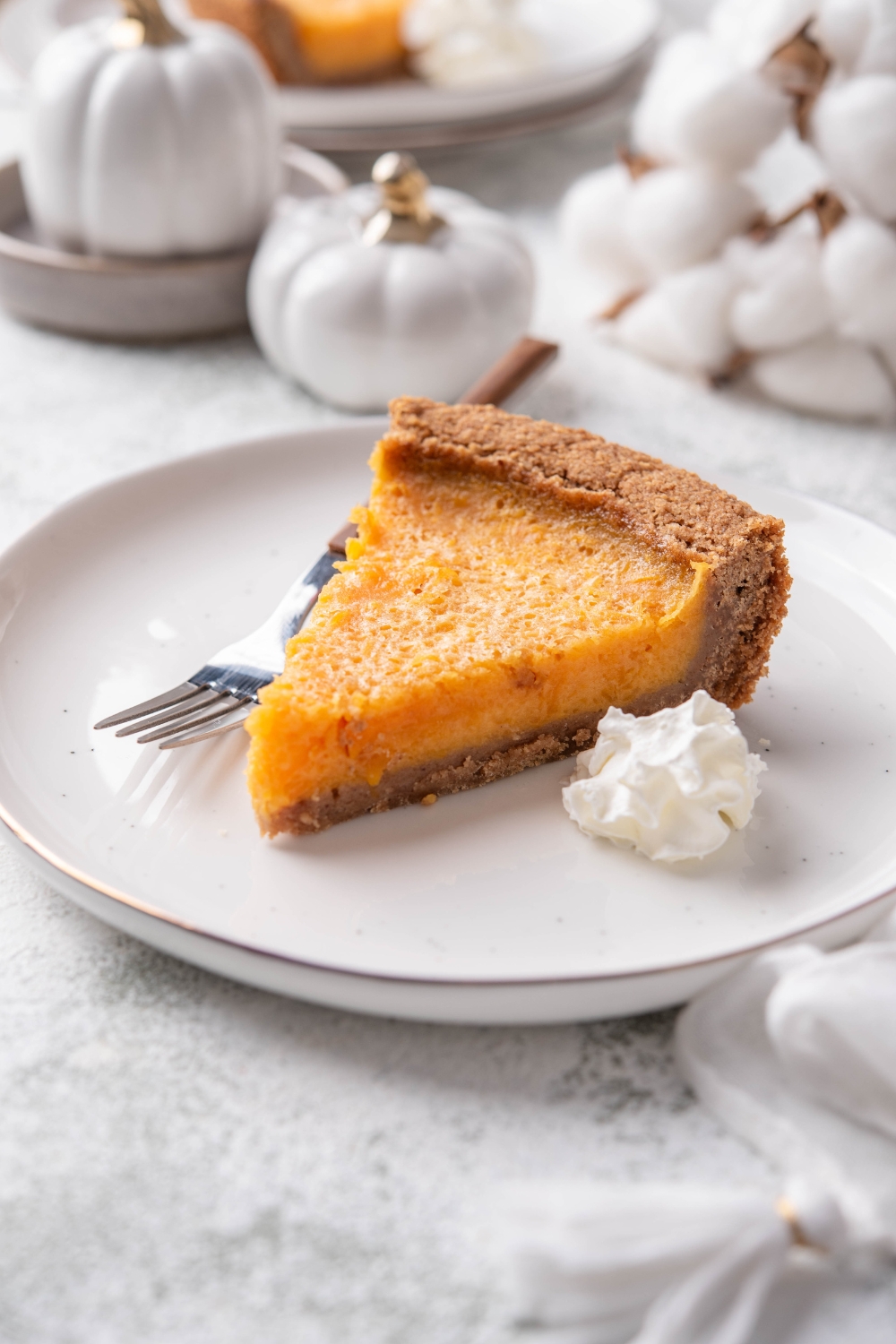 A slice of pumpkin pie on graham cracker crust with a dollop of whipped cream and a fork on the plate.