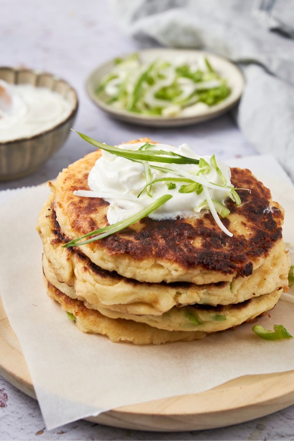 A stack of mashed potato pancakes with sour cream and green onion garnish on a plate.