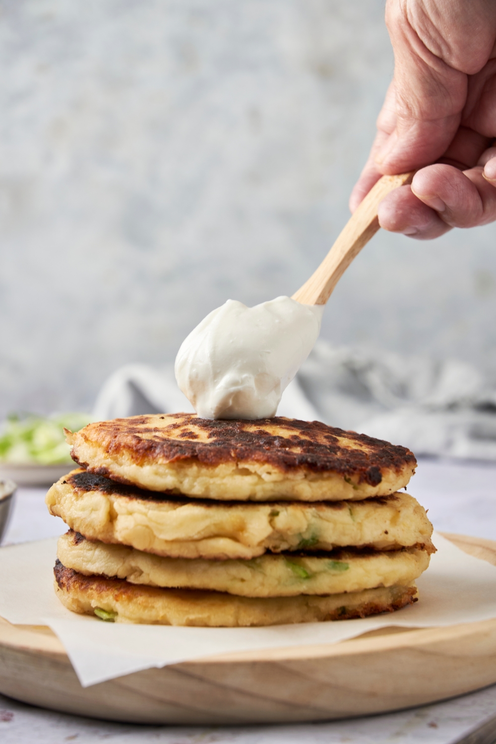 A stack of three mashed potato pancakes. A wooden spoon drops a dollop of sour cream on top.