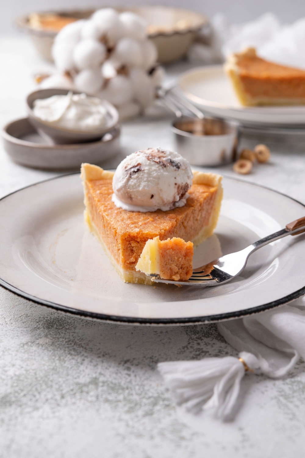 A slice of sweet potato pie topped with whipped cream with a bite missing and a fork is next to the pie slice holding the missing bite.